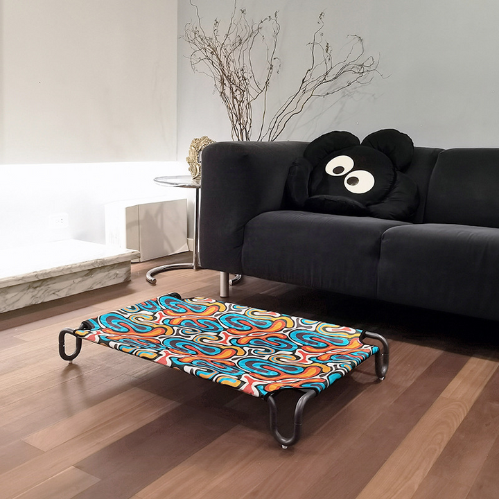 dog cot bed with colorful bed fabric on the wooden floor and beside a black sofa